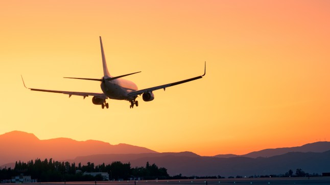 Plane landing at sunset with mountain background.